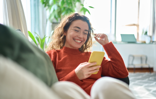 Kobieta siedząca na kanapie i korzystająca ze smartfona w salonie, robiąca na nim zakupy.